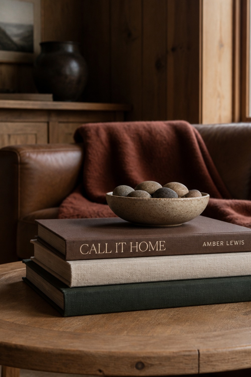 Call It Home by Amber Lewis styled spine-out in a stack of coffee-table books with a stone bowl, on a wood table in a cabin living room