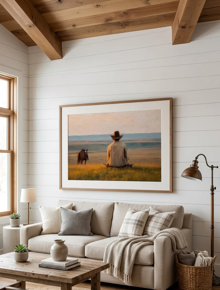 Framed painting of a lone cowboy sitting in a prairie with his horse, over a linen sofa in a farmhouse living room