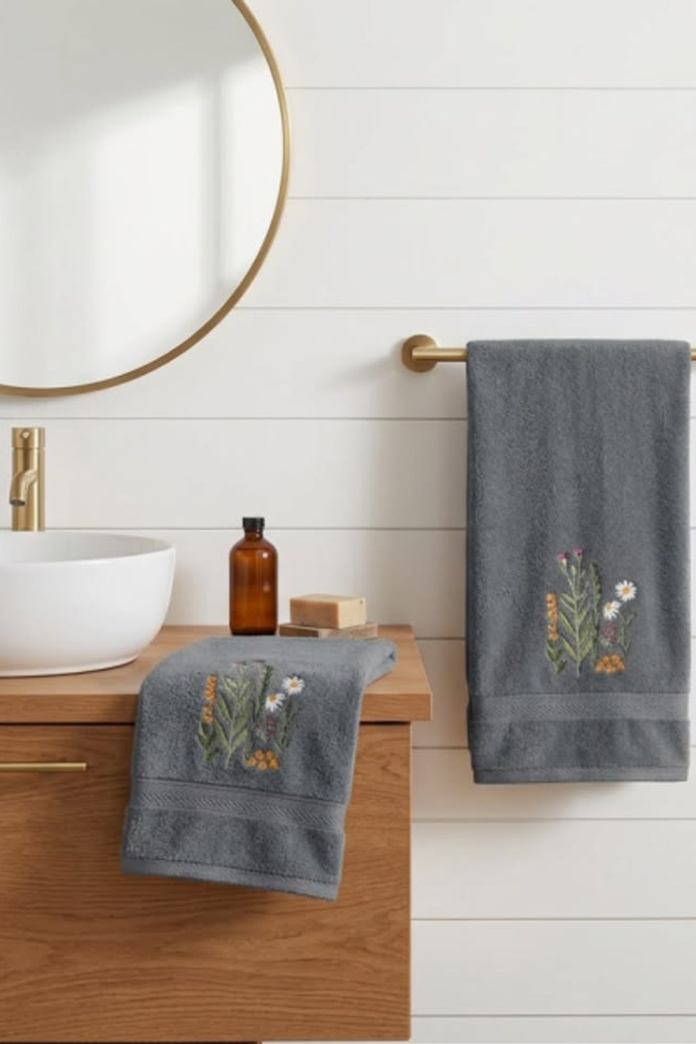 Two gray cotton hand towels with embroidered wildflowers on a brass bar and wood vanity in a white cabin bathroom