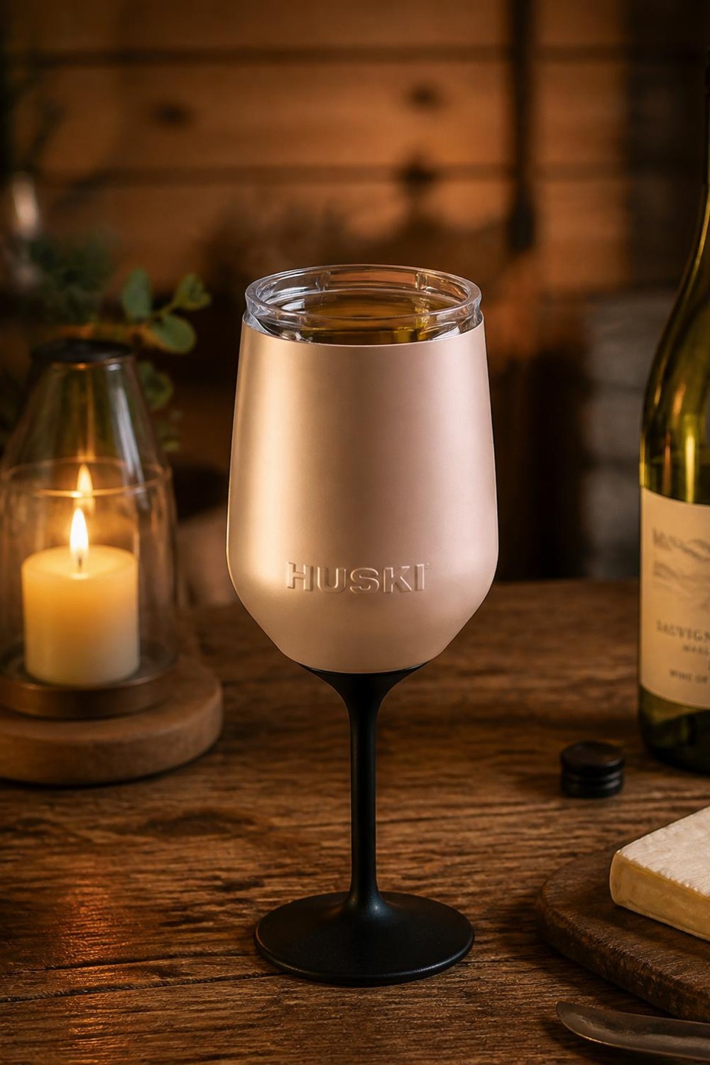 Champagne stainless steel Huski wine tumbler with a detachable black stem on a cabin table beside a candle and wine bottle