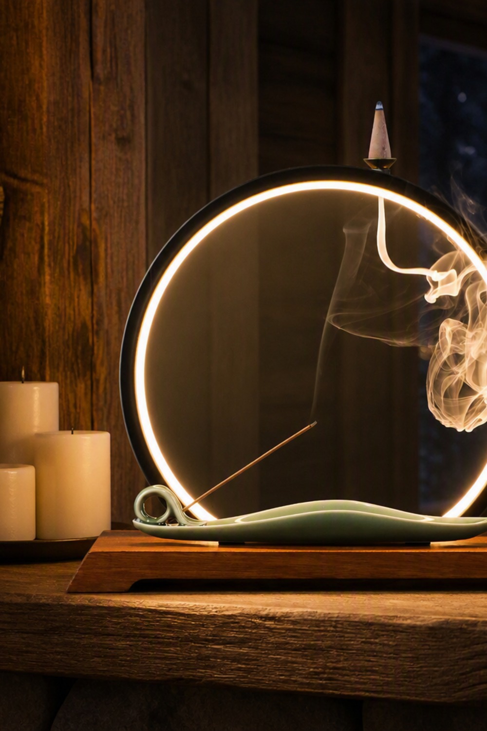 Backflow incense burner with a glowing black LED ring, sage-green ceramic leaf boat, and wood base on a cabin mantel