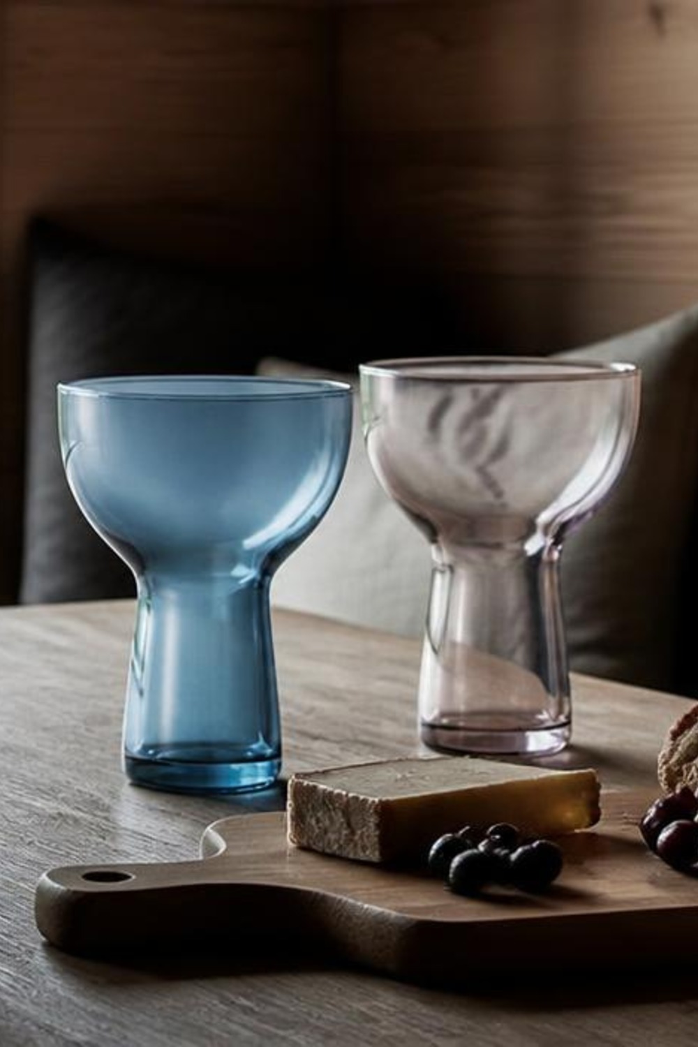 Colored hourglass-shaped tumblers in blue and smoky grey on a cabin dining table with a cheese board