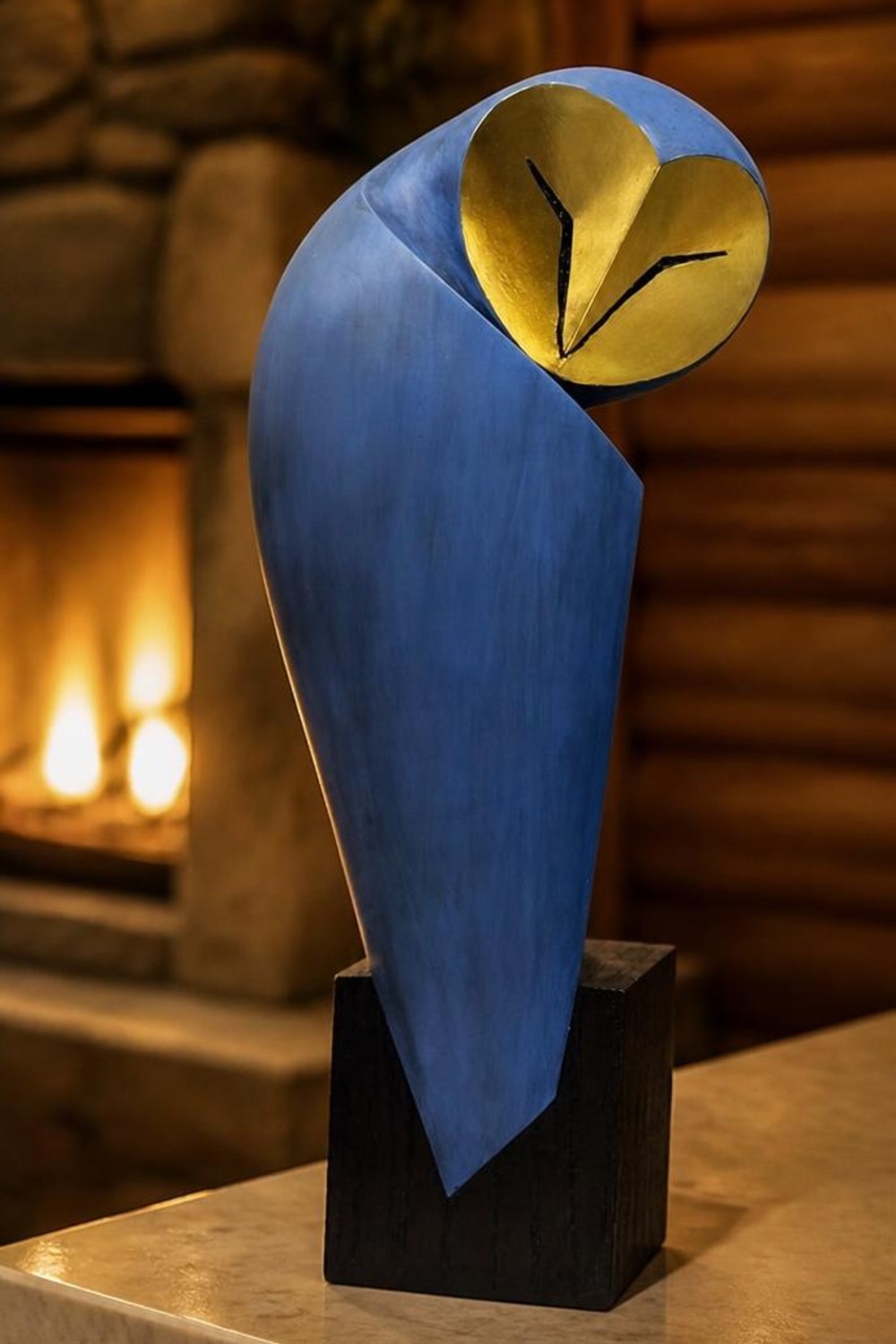 Abstract blue and gold mid-century modern owl sculpture on a mantel beside a cabin fireplace