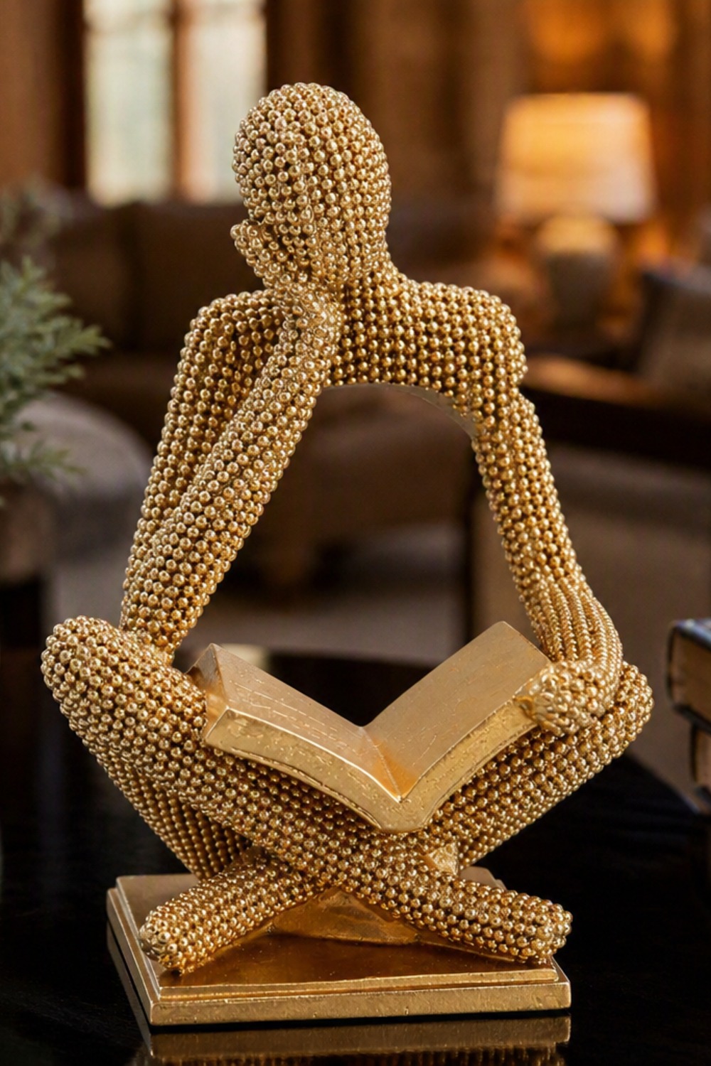 Gold beaded abstract sculpture of a seated figure reading a book on a black side table in a cabin living room