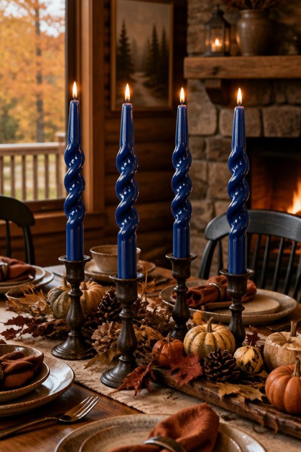 Navy blue spiral-twist taper candles lit in candlesticks on a cabin dining table set for fall