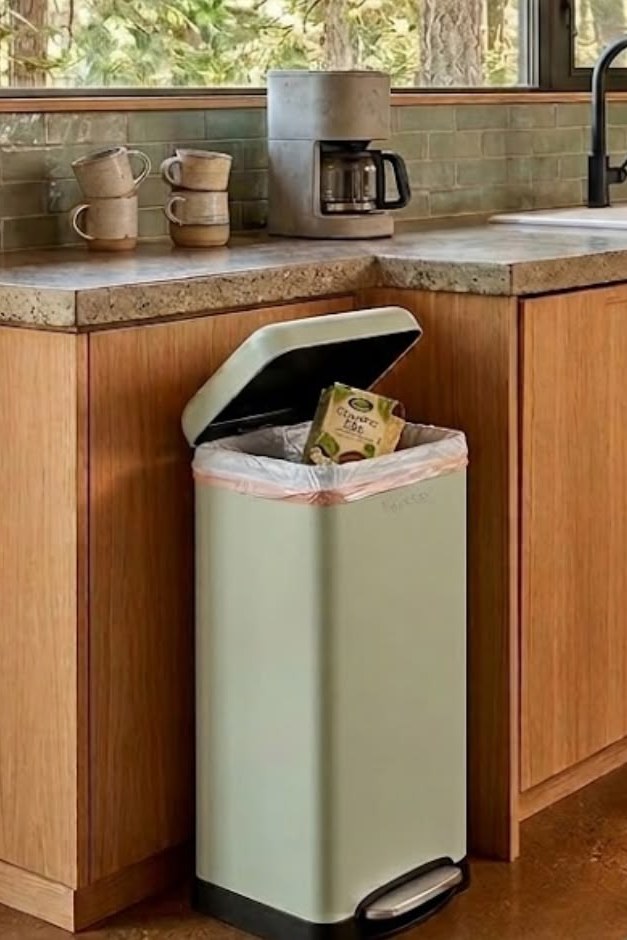 Sage-green retro step trash can beside wood cabinets in a modern cabin kitchen