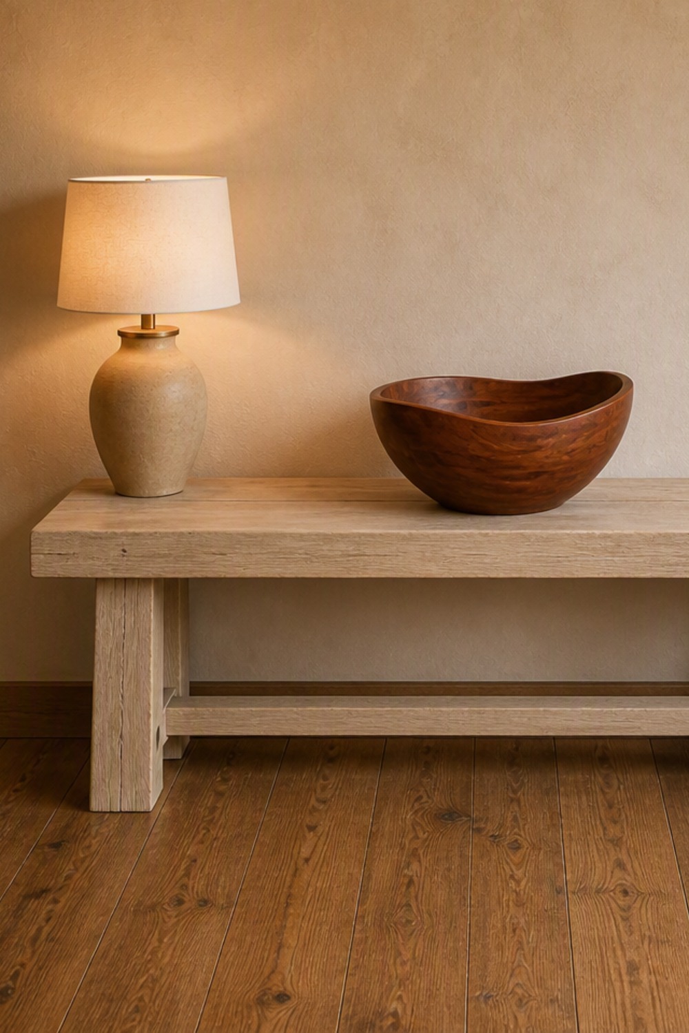 Large cherry-stained wooden bowl with a wavy rim on a pale oak console table beside a table lamp in a cabin entry